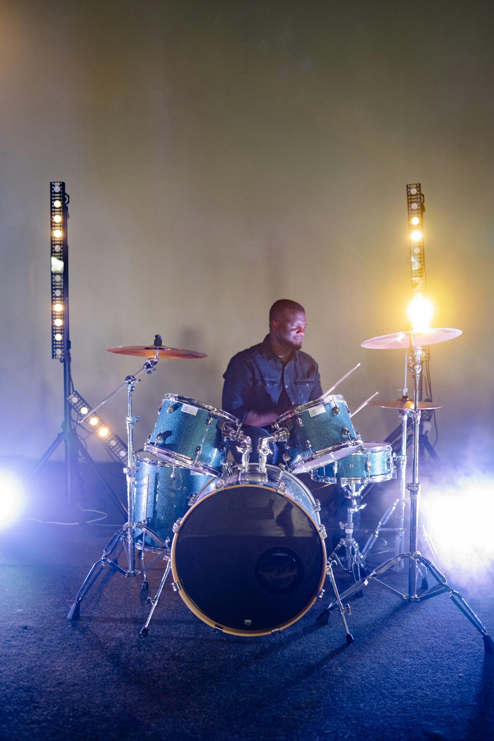 A drummer performing on stage with illuminated drums and dynamic spotlights.